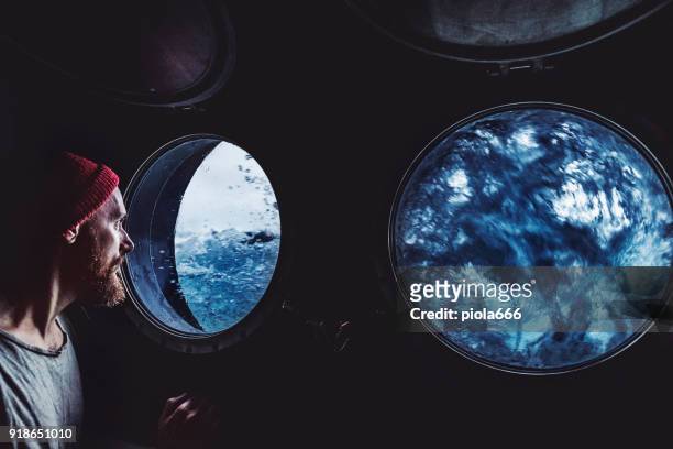 man at the porthole window of a vessel in a rough sea - port hole stock pictures, royalty-free photos & images
