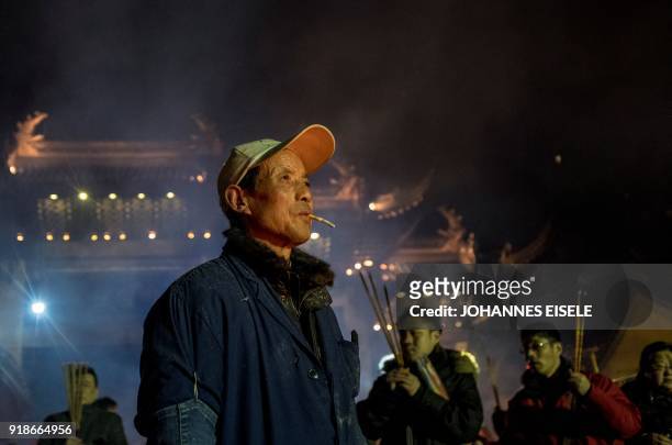 Man smokes a cigarette as people pray with incense sticks to celebrate the Lunar New Year, marking the Year of the Dog, at the Longhua temple in...