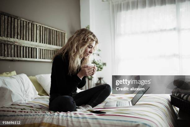 woman using laptop computer sitting on bed at home - real people computer stock pictures, royalty-free photos & images