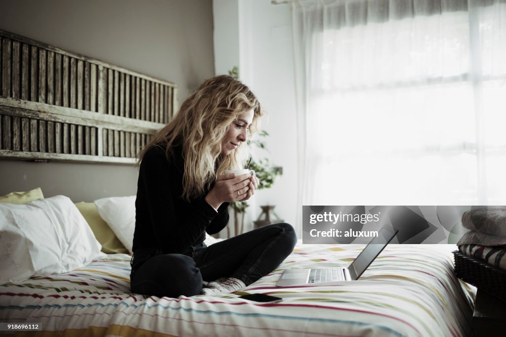 Mulher usando o computador portátil, sentada na cama em casa