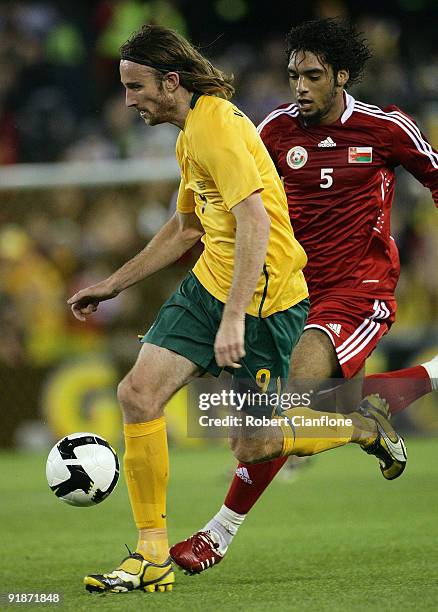 Josh Kennedy of Australia keeps the ball ahead of Mohammed Addullah of Oman during the Asian Cup Group B qualifying match between the Australian...