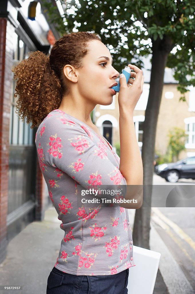 Young woman using asthma inhaler on road