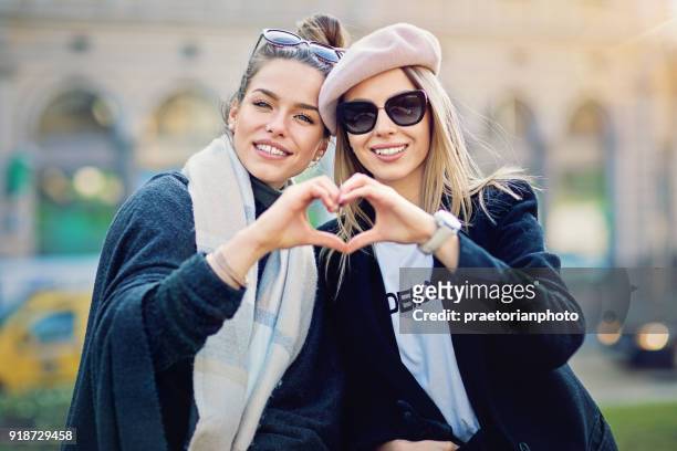 two girlfriends are making heart with their hands on the street - hands in heart shape stock pictures, royalty-free photos & images