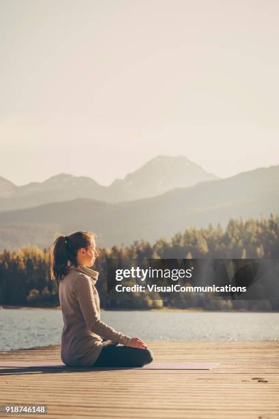 young woman practicing yoga on dock by the lake. - meditation relaxation stock pictures, royalty-free photos & images