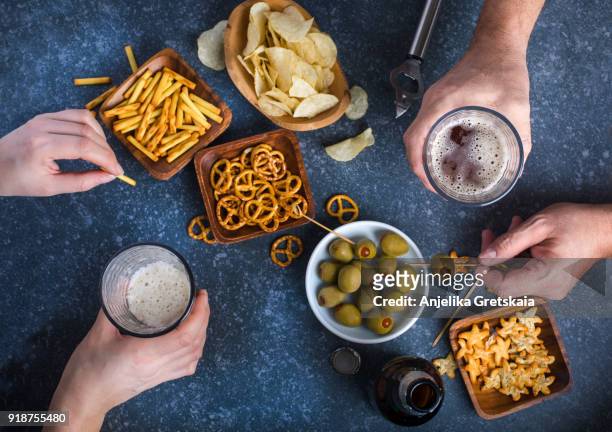 hands holding glasses with beer on a table. couple drinking beer and eating snacks - snack foto e immagini stock