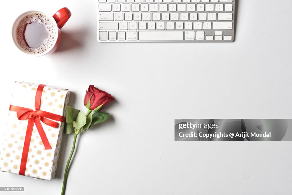 Flat lay Valentines Day background with computer keyboard, gift, coffee mug and red tulip top view white copy space