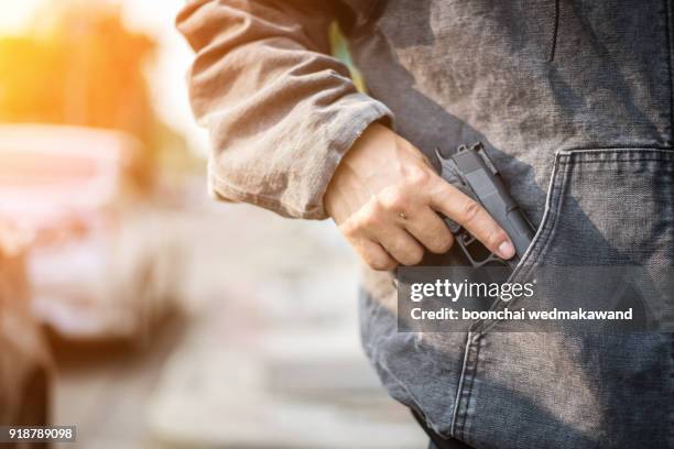 armed man (attacker) holds pistol in public place. many people on street. gun control concept. - pistool handwapen stockfoto's en -beelden