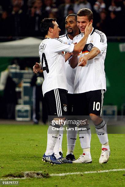 Lukas Podolski of Germany celebrates after scoring his team's first goal with team mate Cacau and Piotr Trochowski of Germany during the FIFA 2010...
