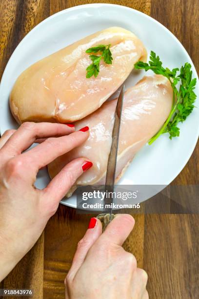 cropped hand of woman cutting raw chicken breast. - hoja de aluminio fotografías e imágenes de stock