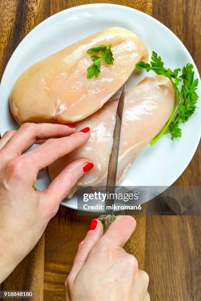 cropped hand of woman cutting raw chicken breast. - hoja de aluminio fotografías e imágenes de stock