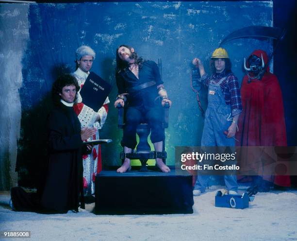 Posed group portrait of Motorhead in mock execution scene with Lemmy sitting in an electric chair in 1984. Left to Right: Pete Gill, Phil Campbell,...