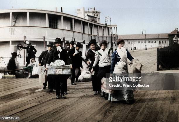 Immigrants to the USA landing at Ellis Island, New York, c1900. They head for the processing centre, each carrying a paper with an entry number which...