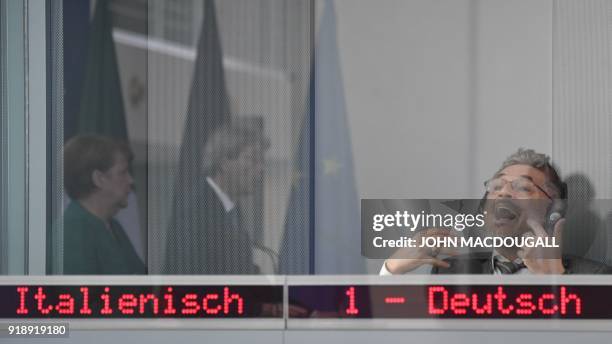The German to Italian interpreter gestures as he translates Italian Prime Minister Paolo Gentiloni who is seen in the reflection of a window with...