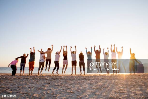 friends jumping in a line on the beach in sunlight - はずむ ストックフォトと画像