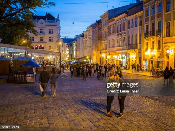 Tourists at sunset on Rynok or Market Square, the main square in the old town of Lviv, in Ukraine. Its well preserved architecture, which blends...