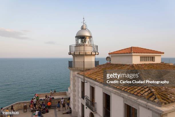 tourists seated in front of the lighthouse of peniscola, costa del azahar, spain - costa_del_azahar stock pictures, royalty-free photos & images