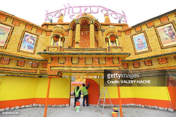 Workers apply a coat of paint on a structure beneath a sculpture made of lemons and oranges are displayed on the eve of the 85th Lemon Festival, on...