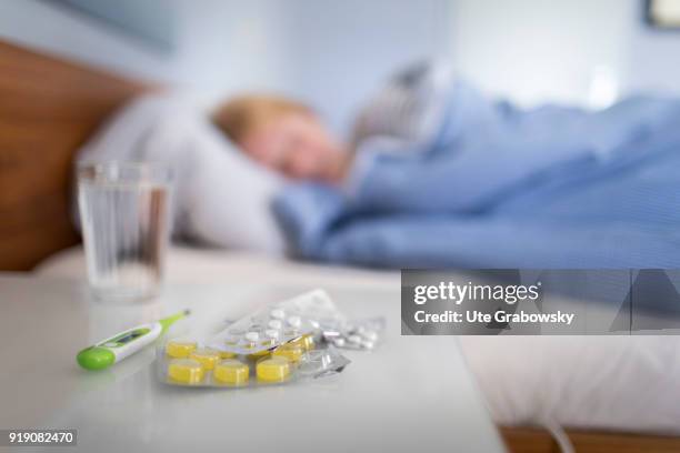 Bonn, Germany Posed Scene: Tablets lie on a table while a sick woman lies in bed in the background on February 13, 2018 in Bonn, Germany.