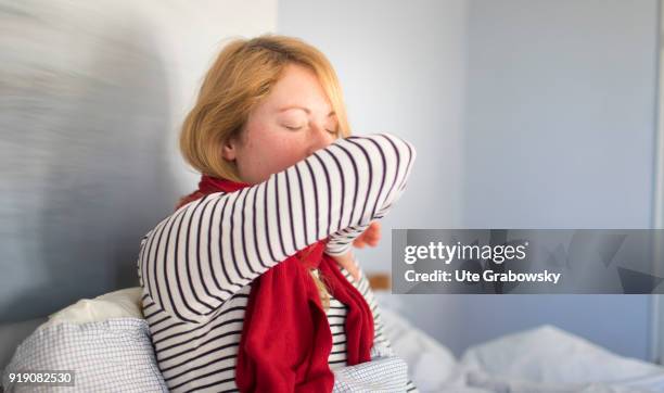 Bonn, Germany Posed Scene: A sick woman lies in bed and coughs in the crook of her arm on February 13, 2018 in Bonn, Germany.