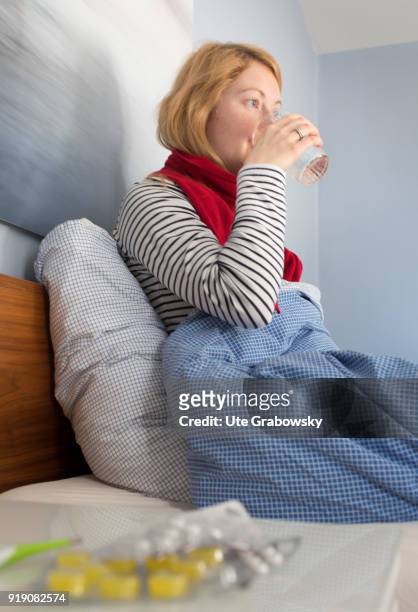 Bonn, Germany Posed Scene: A sick woman is sitting in bed and drinking water on February 13, 2018 in Bonn, Germany.