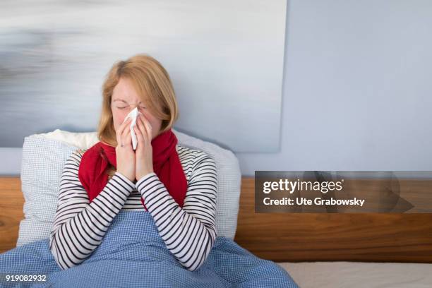 Bonn, Germany Posed Scene: A sick woman sits in bed and cleans her nose on February 13, 2018 in Bonn, Germany.