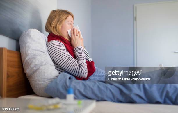 Bonn, Germany Posed Scene: A sick woman sits in bed and cleans her nose on February 13, 2018 in Bonn, Germany.