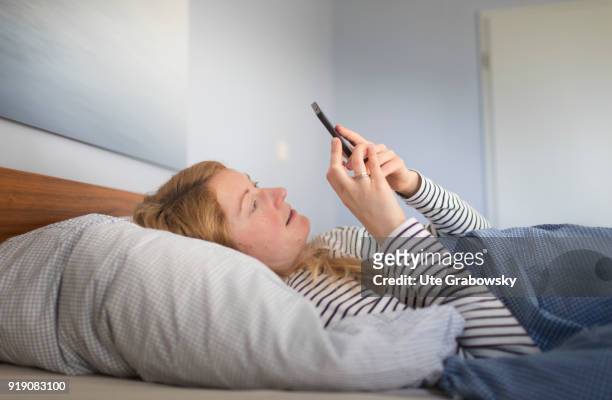 Bonn, Germany Posed Scene: A young woman is lying in bed looking at her smartphone on February 13, 2018 in Bonn, Germany.