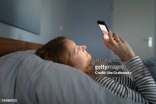 Posed Scene: A young woman is lying in bed looking at her smartphone on February 13, 2018 in Bonn, Germany.