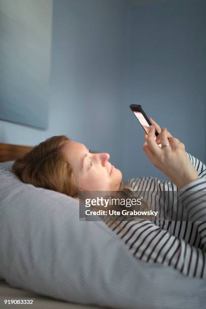 Posed Scene: A young woman is lying in bed looking at her smartphone on February 13, 2018 in Bonn, Germany.