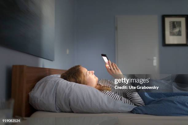 Bonn, Germany Posed Scene: A young woman is lying in bed looking at her smartphone on February 13, 2018 in Bonn, Germany.