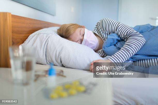 Posed Scene: A sick woman lies in bed wearing a surgical mask on February 13, 2018 in Bonn, Germany.