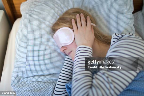 Posed Scene: A sick woman lies in bed wearing an eye mask on February 13, 2018 in Bonn, Germany.