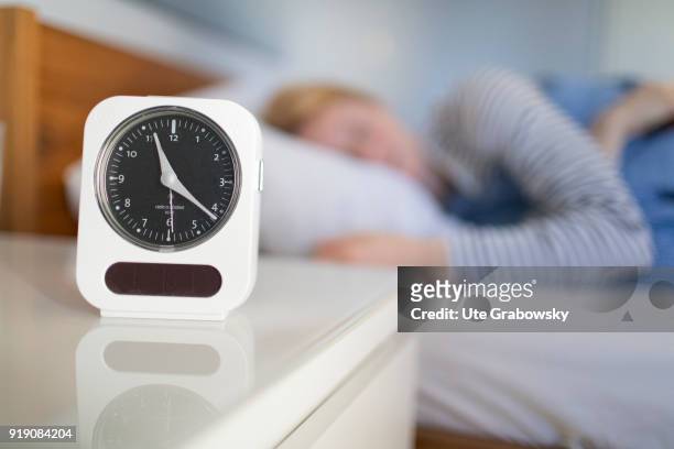Bonn, Germany Posed Scene: An alarm clock stands on a bedside table while a woman is sleeping in bed on February 13, 2018 in Bonn, Germany.