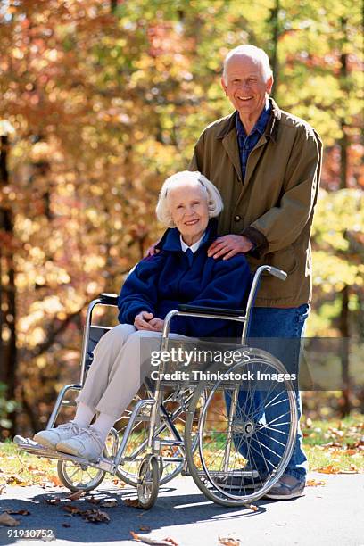 portrait of mature woman in wheelchair and husband standing behind her - gay en silla de ruedas fotografías e imágenes de stock