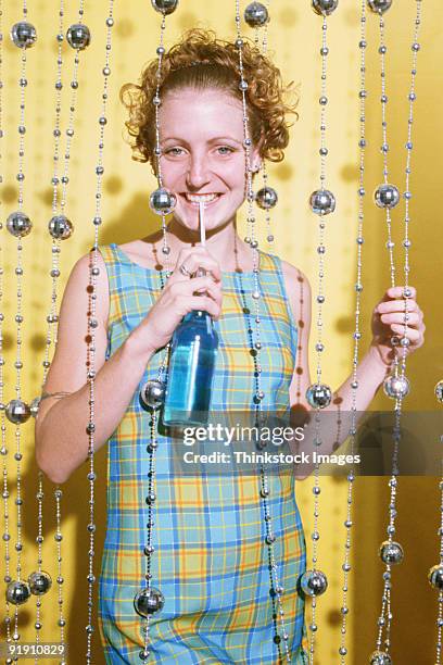 young woman in beaded curtain, straw to lips, holding  liquid in bottle - straw lips stock pictures, royalty-free photos & images