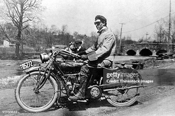 rakish motorcyclist sitting on bike,1909 man and woman standing in background - vintage motorcycle stockfoto's en -beelden