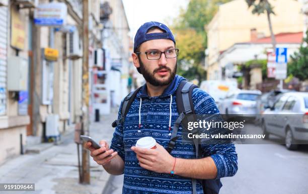 giovane con smartphone e caffè per strada - beard men street foto e immagini stock