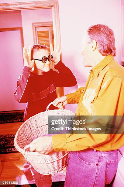 father, holding laundry basket, talking to son, wearing geeky glasses and making face at father, in laundry room - man washing basket child stock pictures, royalty-free photos & images