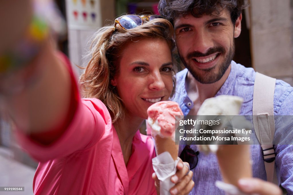 Smiling couple eating ice cream cones taking selfie on street in Barcelona