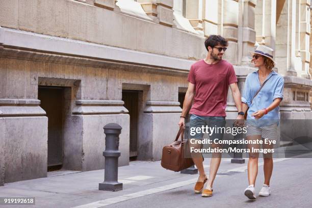 smiling couple walking with luggage on street in barcelona - pantalón corto gris fotografías e imágenes de stock