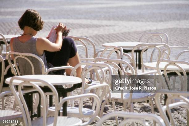 Woman reading in a terrace A woman reads a magazine seated in the terrace of a bar