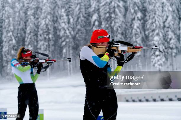 side view of two female athletes practicing target shooting in snowstorm - biathlon ski stock pictures, royalty-free photos & images