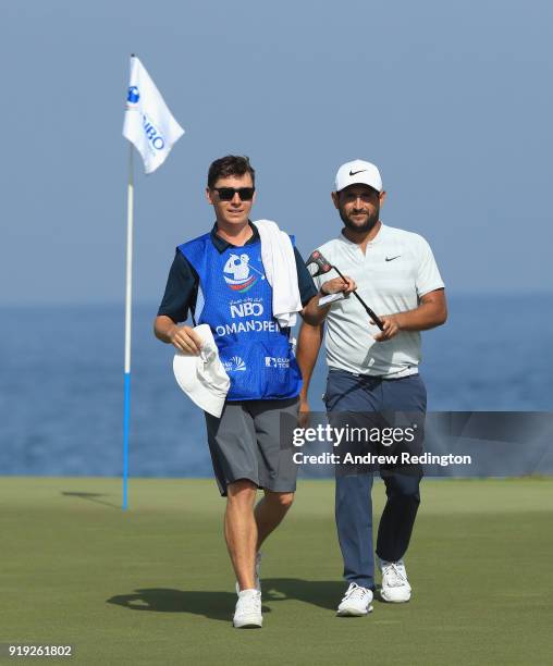 Alexander Levy of France walks off the 18th green with his caddie Tom Ayling during the third round of the NBO Oman Open at Al Mouj Golf on February...