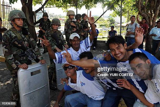 Fans of the Honduran national football team pose for a picture in front of soldiers standing guard outside the presidential palace in Tegucigalpa on...