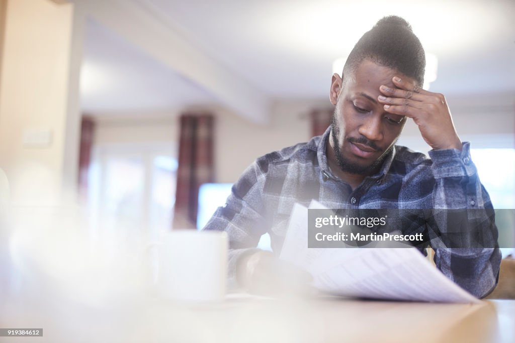 Worried young male reading through bank statements