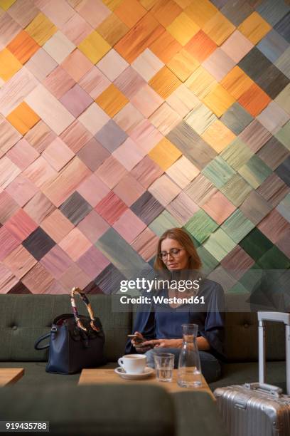 portrait of businesswoman with baggage in a cafe looking at cell phone - multi colored purse ストックフォトと画像