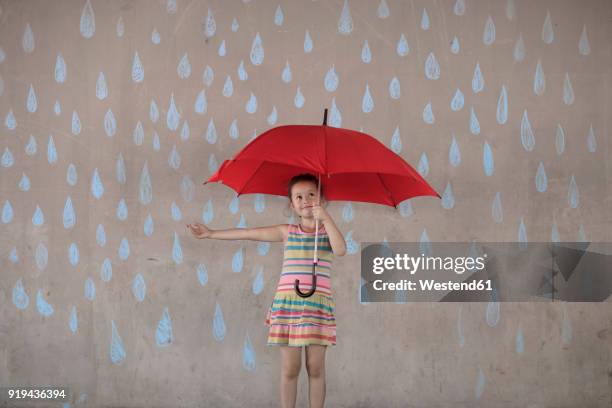 girl holding a red umbrella standing next to a concrete wall with rain drop chalk drawings - chalk wall ストックフォトと画像