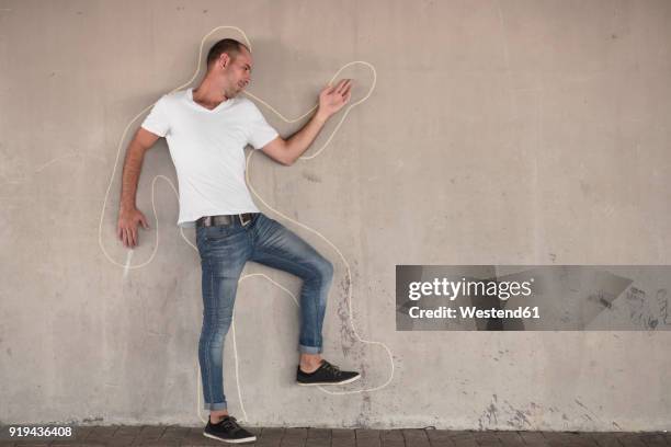 man pretending to be dead standing with chalk outline drawn on concrete wall - chalk wall ストックフォトと画像