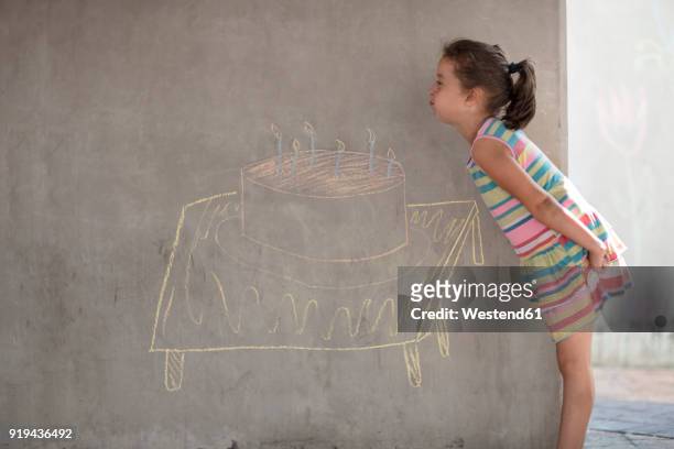girl pretending to blow out chalk birthday cake and candle drawing on concrete wall - chalk wall ストックフォトと画像