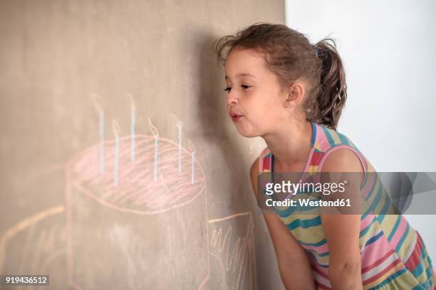 girl pretending to blow out chalk birthday cake and candle drawing on concrete wall - chalk wall ストックフォトと画像